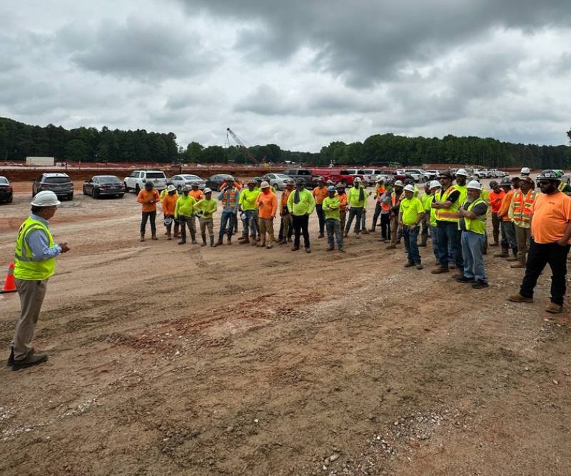 A group of construction workers gather around a project manager at a job site.