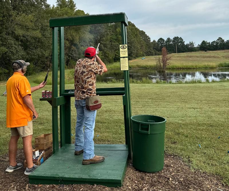 A man holds a rifle and shoots at a clay flying over a lake