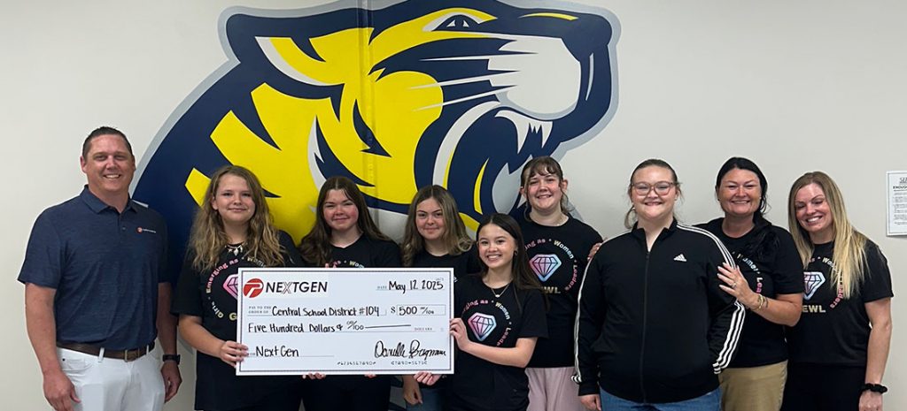 2025_901-ng-comm-impact_main Teachers and students holding a large check in front of a painting of a tiger