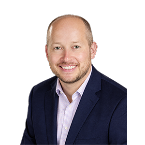 A smiling man with a scruffy beard, lavender collared shirt, and navy sports coat