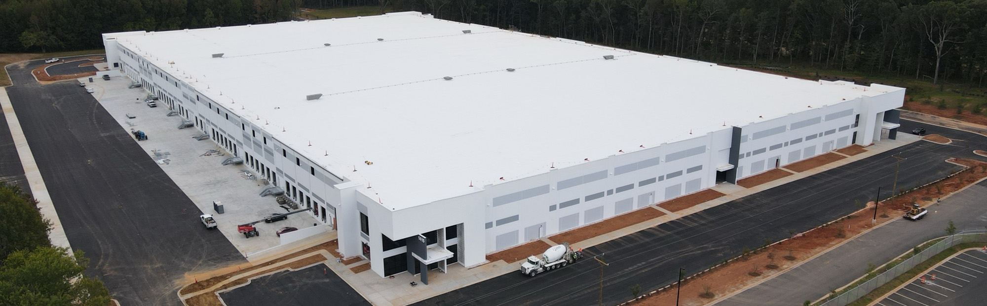 ILC Phase 2_Website Hero_2000x621 (2) A large white distribution center with a concrete mixer parked outside