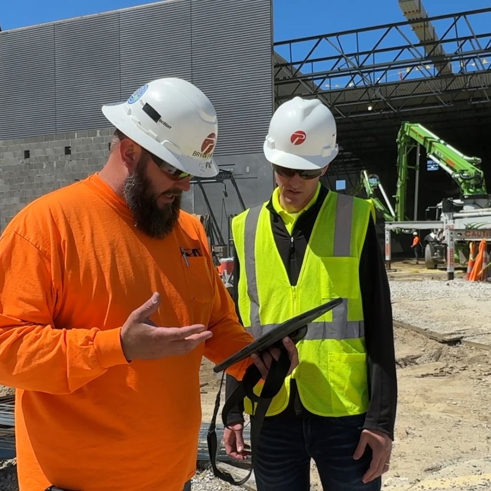 poettker-construction-approach-project-management two men in construction hats and high-visibility shirts examine an ipad