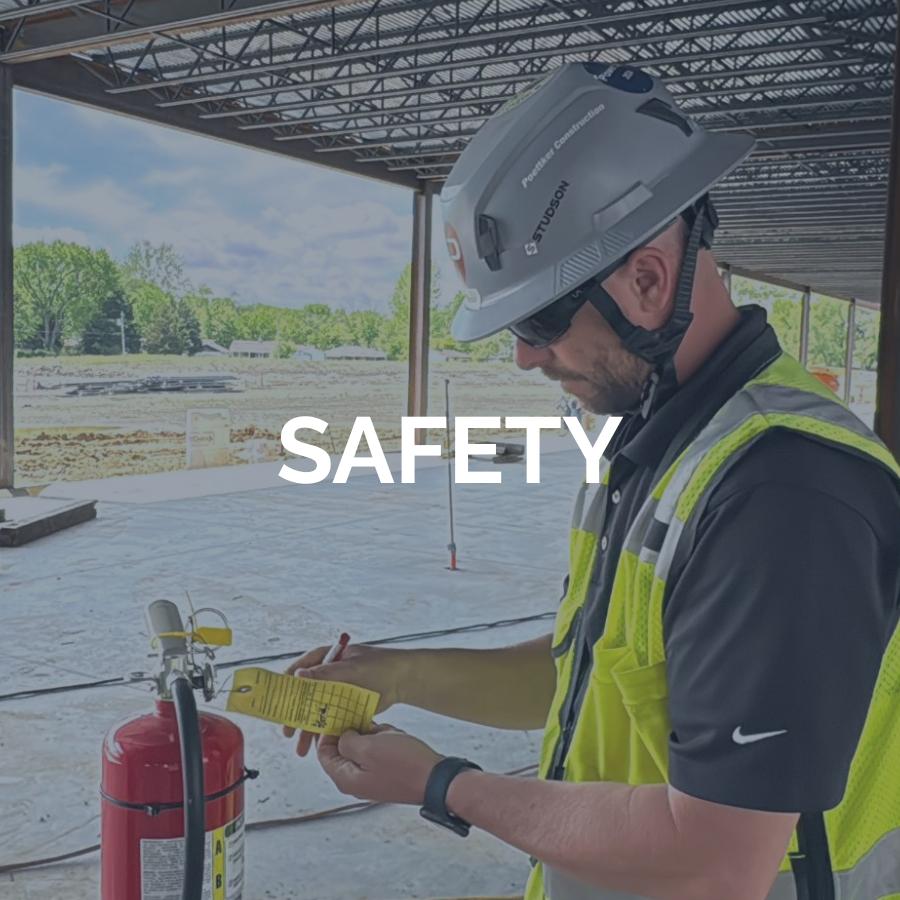A man in a construction vest and helmet inspects the tag on a fire extinguisher