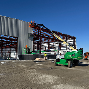 Three construction workers installing metal panels for the exterior of a large building