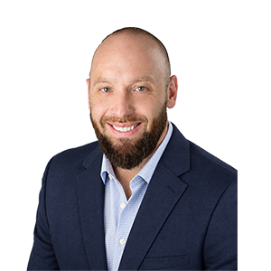 A smiling bald man with a thick beard, collared shirt, and a navy sports coat