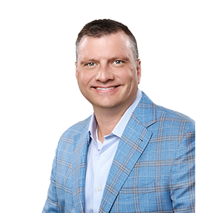 A smiling man with short dark hair and a plaid light blue blazer