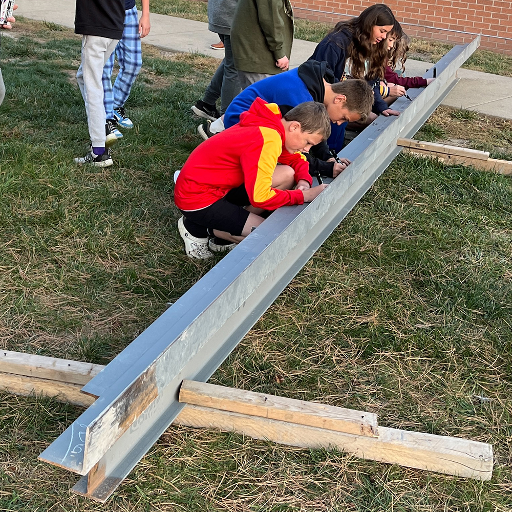 Mascoutah MS Add & Reno 2024_901 NG_2024-10-28_Beam Signing (1) Middle school students squat next to a beam to sign it