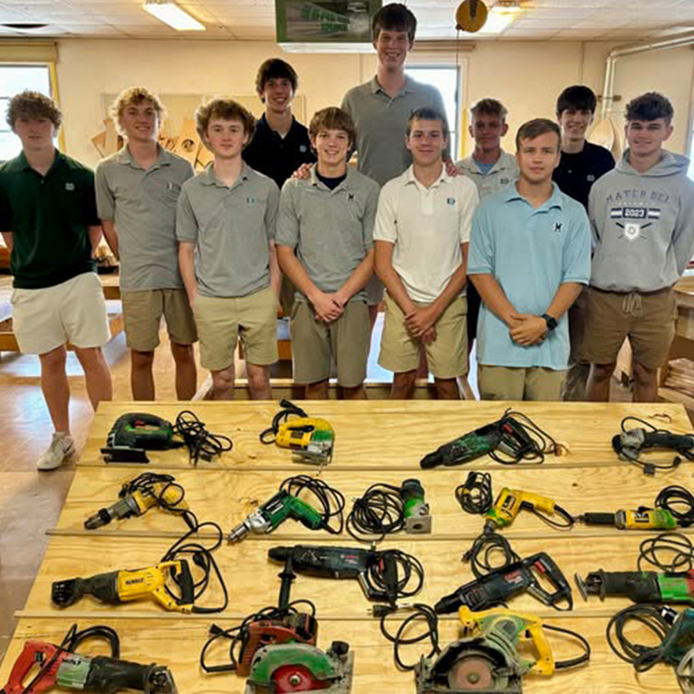 Mater Dei HS Tool Donation-2024-09 A teacher and male high school students stand behind a table filled with power tools