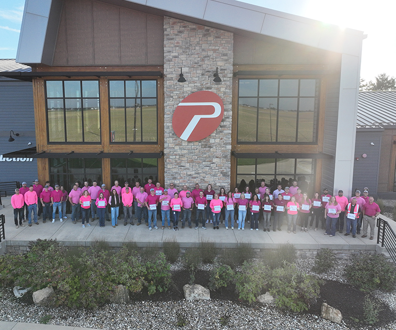 A large group of men and women wearing pink shirts outside a corporate headquarters