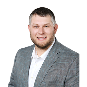 A smiling man with a beard in a collared white shirt and plaid sports coat
