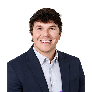 A smiling man with dark brown hair, a gray collared shirt, and a navy sports coat
