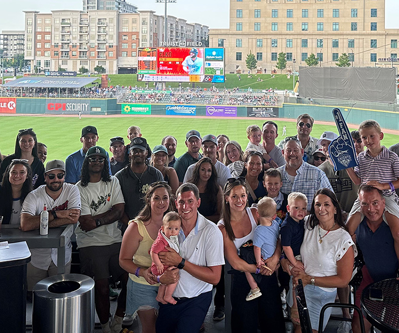 A group of men, women, and children in a party box at a baseball game