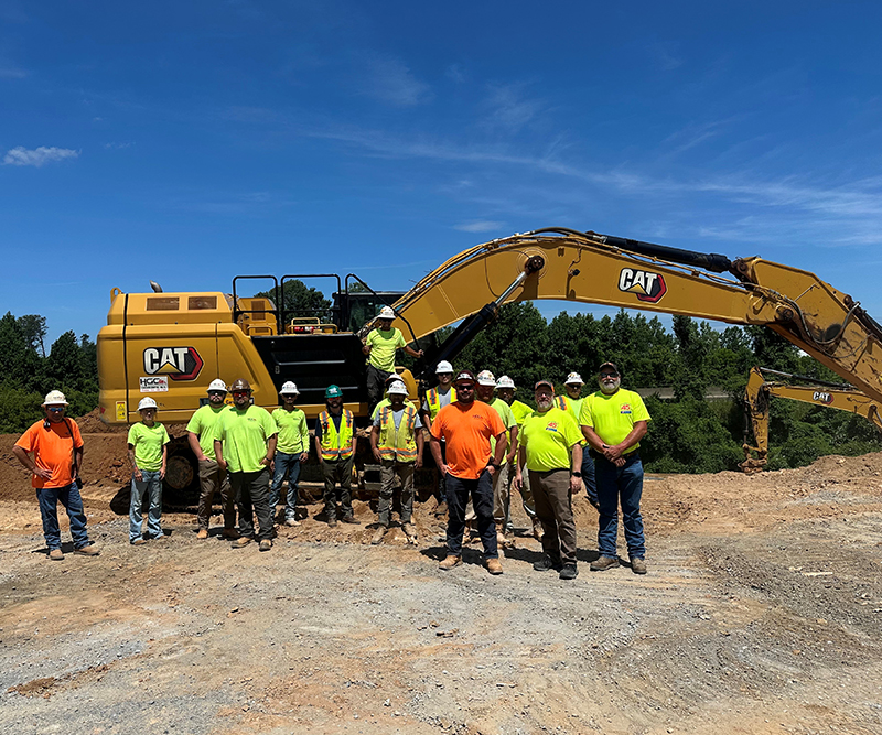 A group of construction workers standing in front of a piece of machinery at a construction site