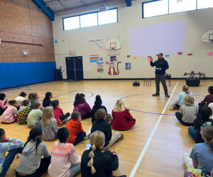 A man standing in front of a drone addresses a gym full of students