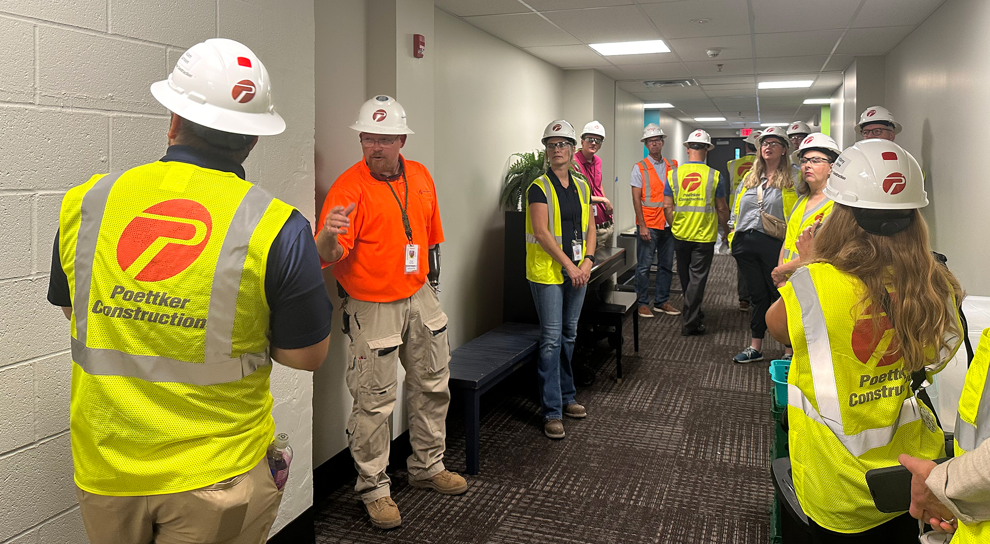 A group of men and women in hard hats and high-visibility vests in a hallway