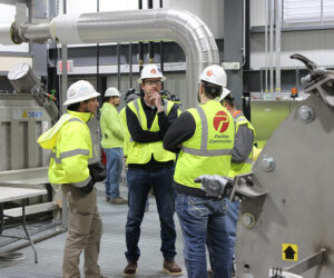 Four men in high-visibility and hard hats conversing in an industrial space