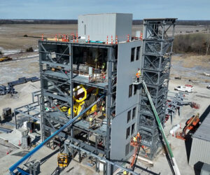 A multi-story manufacturing facility under construction with two cranes