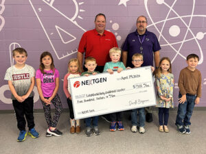 A group of children holds an oversized check next to two men in front of a purple wall