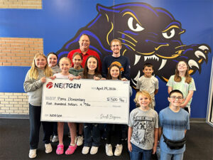 Two men stand behind a group of students holding a large check in front of a wall with a blue panther
