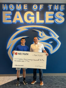 A high school student in a blue shirt accepts an oversized check from a man in a white shirt