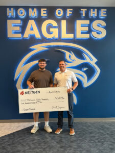 A smiling man presents an oversized check to a high school senior in a brown shirt
