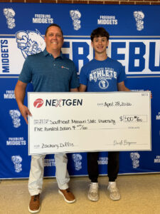 A man in a blue shirt bestows an oversized check to a high school boy