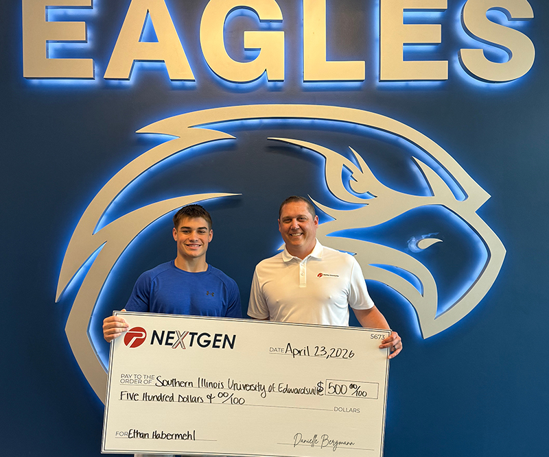 A high school student and a man hold an oversized check in front of an Eagles emblem on the wall