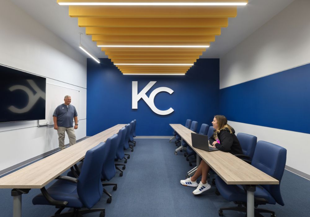KC Gym Add_Website Body_1000x700 (4) media room with two long tables, blue chairs and KC on a blue wall