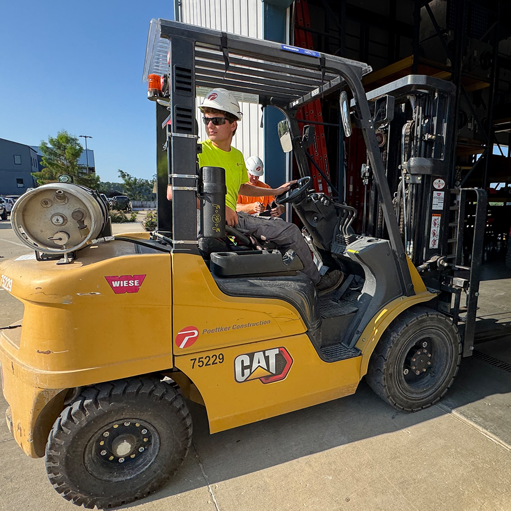 A man in a hard hat backs up a forklift
