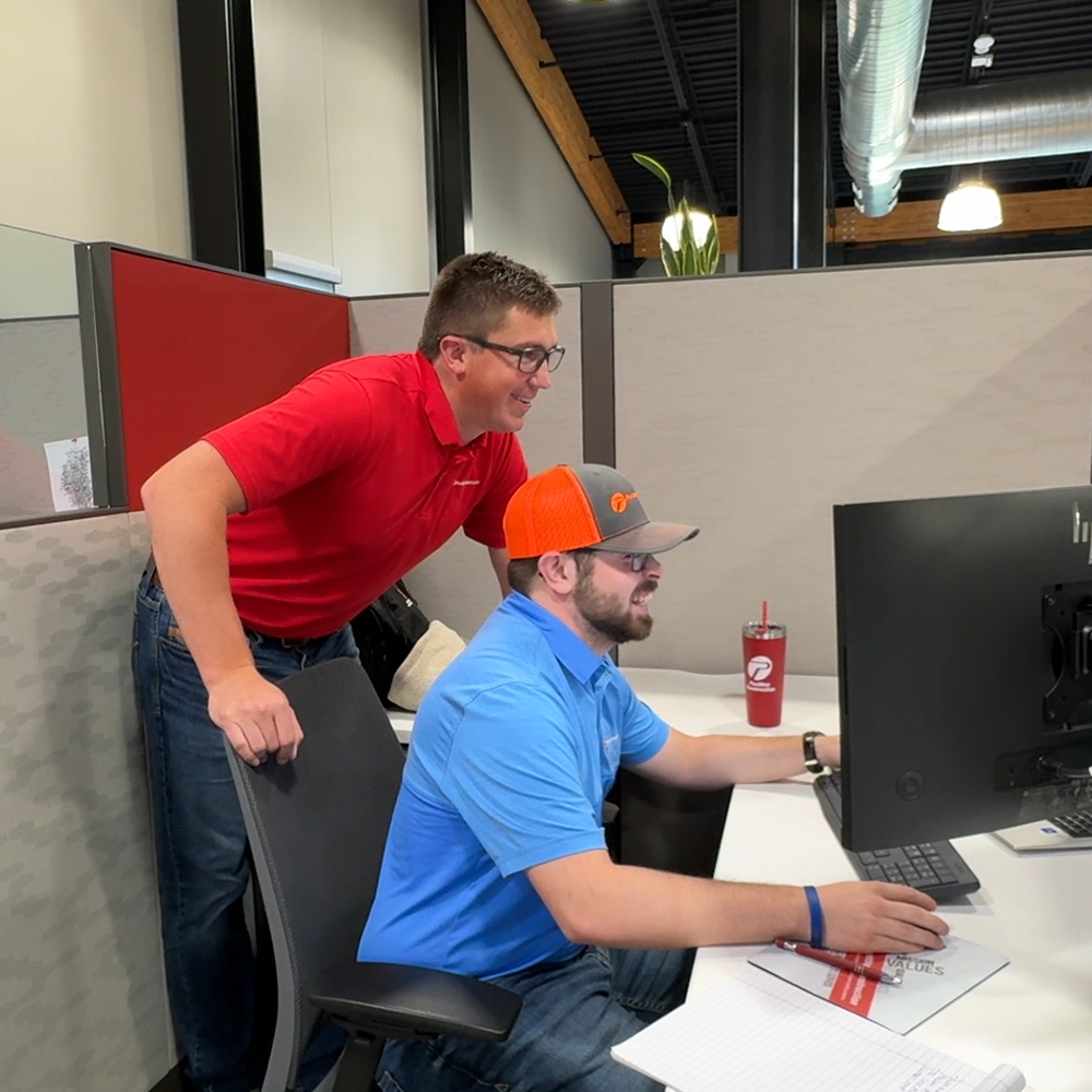 Two smiling men look at computer monitors