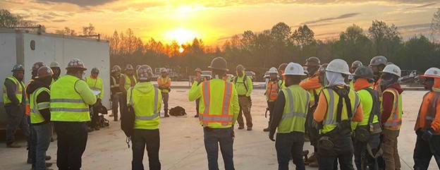 Team-at-Sunrise Construction workers in high visibility vests meeting at a construction site at sunrise