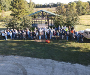 A large group of men and women stand in front of a pavilion 