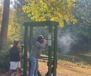 A man at a shooting range holds a rifle with a cloud of smoke around the barrel 