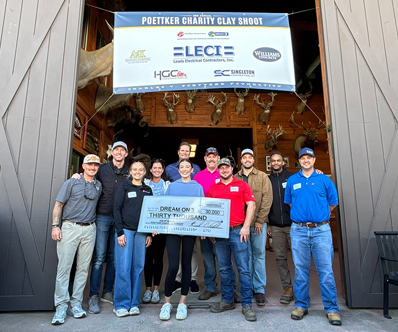 A group of men and women stand in front of a barn holding an oversized check